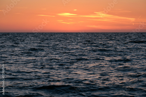 Dramatic bright red sky at ocean sunset, soft evening clouds over sea dark water