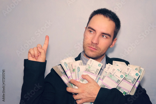 Young man over grey grunge wall, number one. guy in the suit and the money in his hands points his finger up. Good business idea