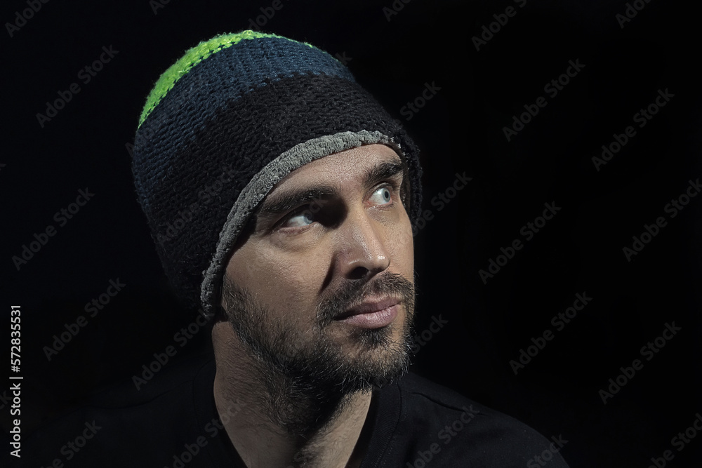 Portrait of a handsome man wearing a hat and black t-shirt on a black background. Dramatic portrait of a handsome, middle-aged white man. Head turned to the side. Portrait of a handsome man wearing a hat and black t-shirt on a black background. Dramatic portrait of a handsome, middle-aged white man. Head turned to the side.