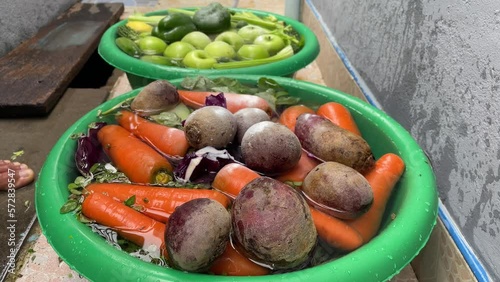 Pouring baking soda power (Sodium bicarbonate) to wash pesticide from freshly green fruits and vegetables, carrot, beetroot, apple in green plastic enamel bowl. 