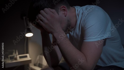 Bad thoughts and dreams. Upset young caucasian man presses his hands to his head and cannot sleep in bed at night. Side effects of coronavirus insomnia, depression and melancholy. Sleep disorder.