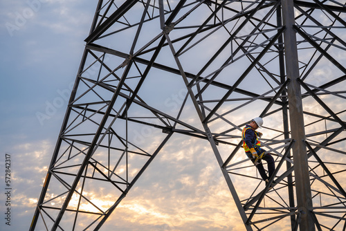 A technician or worker are using safety harnesses to climb high-voltage pylons for inspection and maintenance at high-voltage pylon stations.