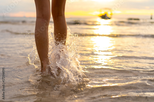 Asian woman legs walking on sea water at tropical island beach at summer sunset. Attractive girl enjoy and fun outdoor lifestyle travel on beach holiday vacation at the sea.