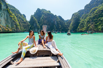 Group of Young Asian woman friends sitting on ship bow and looking beautiful nature of tropical island lagoon. Attractive girl relax and enjoy outdoor lifestyle travel on boat on summer beach vacation