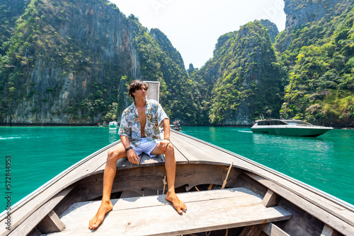 Young Asian man looking beautiful nature of island beach lagoon during travel on boat in summer sunny day. Handsome guy relax and enjoy outdoor lifestyle travel on holiday vacation in Thailand