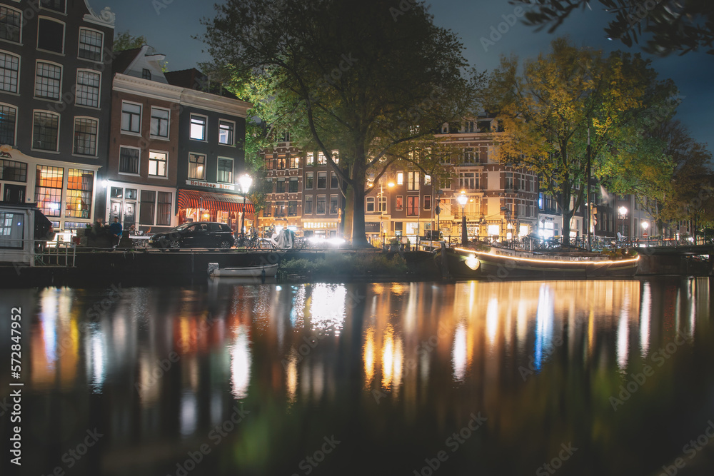 Amsterdam canal, bridge, and medieval houses in the evening, Bright cityscape of Amsterdam with night lights reflection in the water, Night landscape with houses and canal in amsterdam