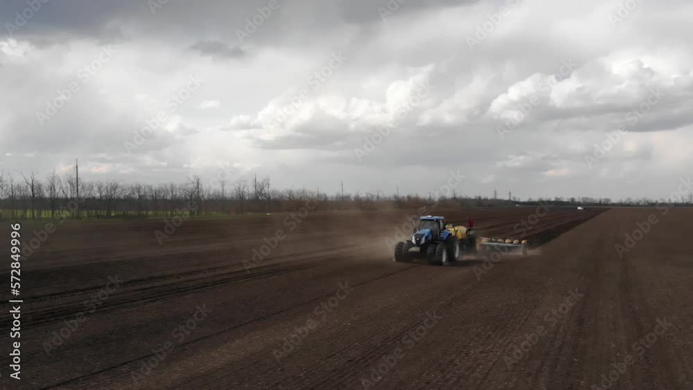 Blue tractror planting sunflower with yellow planter on the cultivated field in Ukraine Blue tractror planting sunflower with yellow planter on the cultivated field in Ukraine