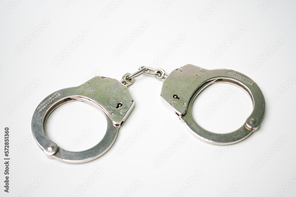 Object is a unilateral handcuff made of iron, single lock, on a white background, symbolizing the law and the offense. Object is a unilateral handcuff made of iron, single lock, on a white background, symbolizing the law and the offense.