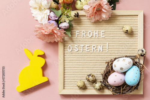 Letter board, Frohe Ostern - Happy Easter in german greeting, Easter eggs and spring flowers on a pastel pink background. View from above.