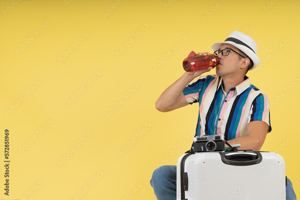 Young man, ready to travel with his camera and passport, sitting on his suitcase, drinking water. Young man, ready to travel with his camera and passport, sitting on his suitcase, drinking water.