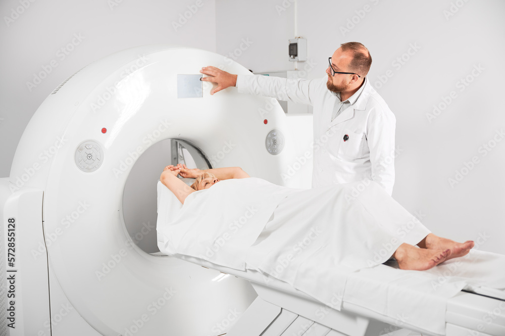 Medical computed tomography or MRI scanner. Male radiologist presses MRI button to examine female patient. Medical computed tomography or MRI scanner. Male radiologist presses MRI button to examine female patient.