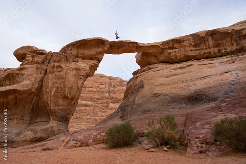 Wadi Rum Desert rock arch with man or woman jumping on the top, popular tourist spot, Wadi Rum, Jordan