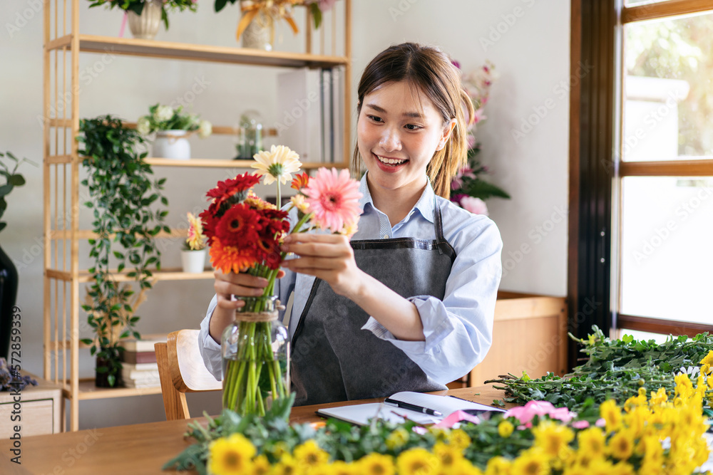 Female florist in apron smiling and arranging gerbera flowers in Female florist in apron smiling and arranging gerbera flowers in