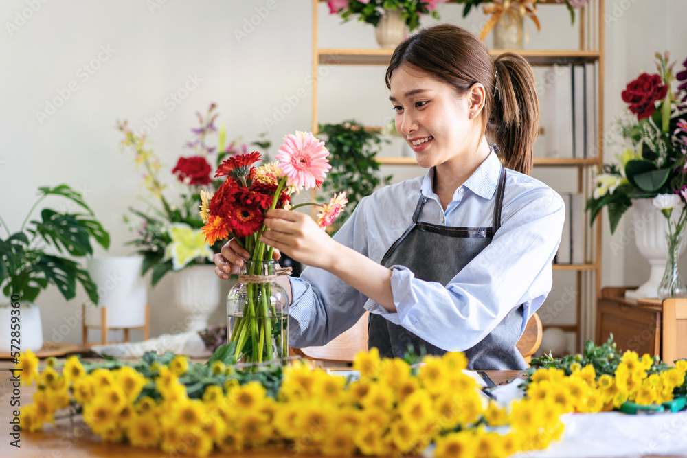 Female florist in apron smiling and arranging gerbera flowers in