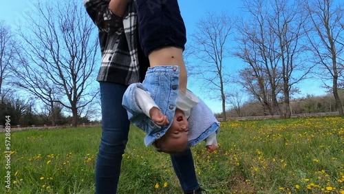 Mother shakes her little daughter upside down over a green lawn