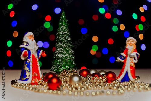 Christmas card with Santa Claus,Snow Maiden.Christmas tree. on a dark background with bright flashing lights of garlands.A statuette, a Santa Claus toy.Christmas tree toys on the Christmas tree. bokeh