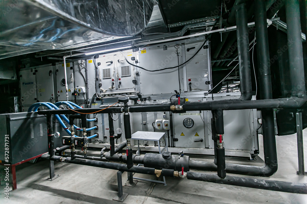 Huge industrial water pump and air handling unit in the ventilation plant room with ductworks and insulated pipelines Huge industrial water pump and air handling unit in the ventilation plant room with ductworks and insulated pipelines