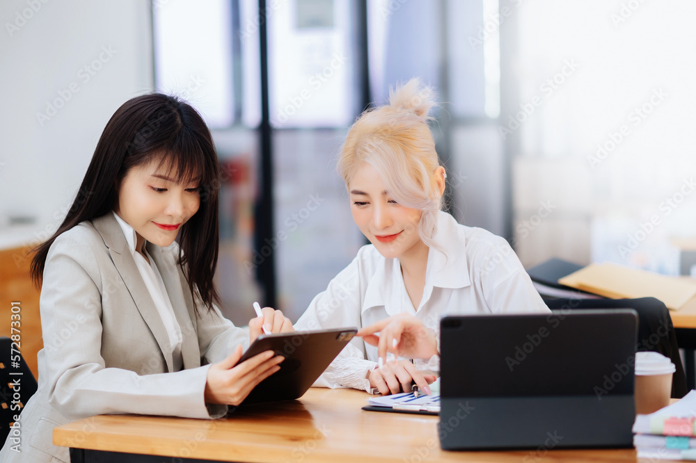 Two Asian businesswoman discuss investment project working and planning strategy with tablet laptop computer in office... Two Asian businesswoman discuss investment project working and planning strategy with tablet laptop computer in office...