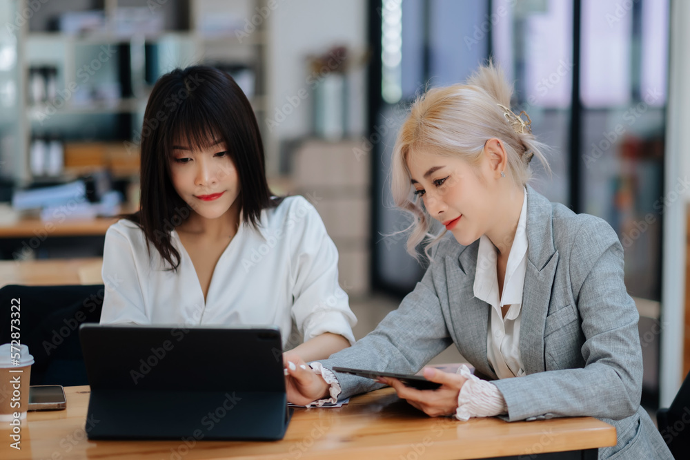 Two Asian businesswoman discuss investment project working and planning strategy with tablet laptop computer in office...