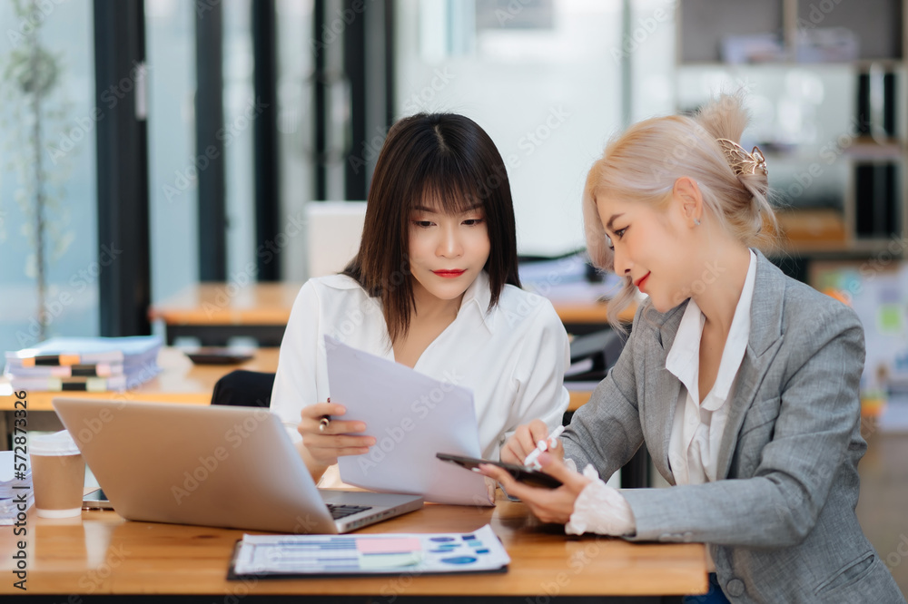 Two Asian businesswoman discuss investment project working and planning strategy with tablet laptop computer in office... Two Asian businesswoman discuss investment project working and planning strategy with tablet laptop computer in office...