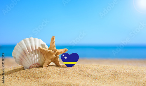 Beautiful beach in the Curacao. Flag of Curacao in the shape of a heart and shells on a sandy beach.