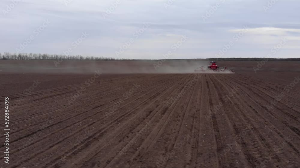 Blue tractror planting sunflower with red planter on the cultivated field in Ukraine Blue tractror planting sunflower with red planter on the cultivated field in Ukraine