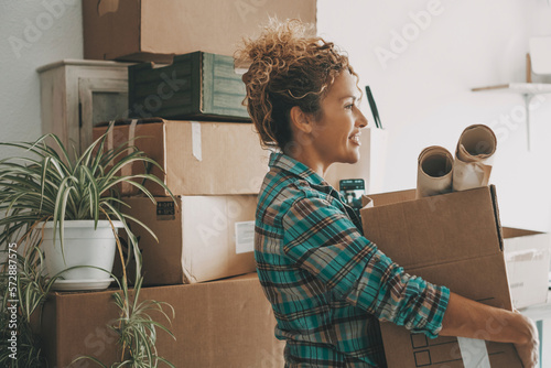 Happy adult woman relocating house lifting cardboard box with life stuffs. New beginnings emotion. Living alone. Modern female people in moving home apartment leisure indoor activity alone. Cheerful