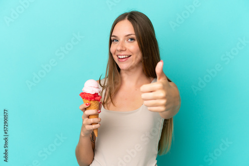 Young Lithuanian woman with cornet ice cream isolated on blue background with thumbs up because something good has happened