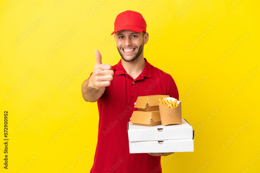 pizza delivery man picking up pizza boxes and burgers over isolated background with thumbs up because something good has happened