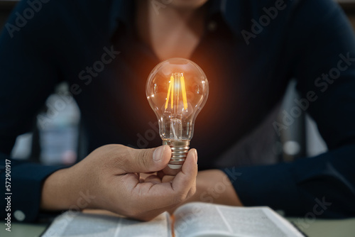 Male hands touching to light bulb which have mechanical gear inside on open book for creative thinking of problem solving and education knowledge concept.