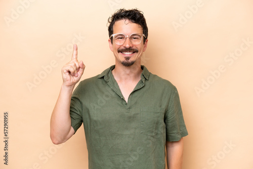 Young caucasian man isolated on beige background pointing up a great idea