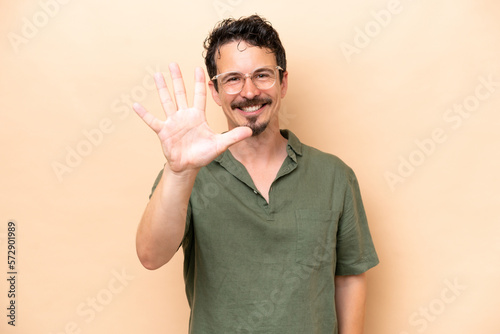 Young caucasian man isolated on beige background counting five with fingers