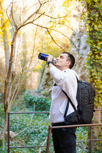 25 year old caucasian young man drinking water from a blue refillable bottle, in the middle of the forest, committed to the environment, travel concept