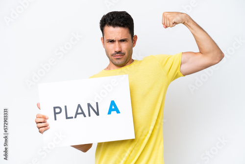 Young handsome man over isolated white background holding a placard with the message PLAN A doing strong gesture