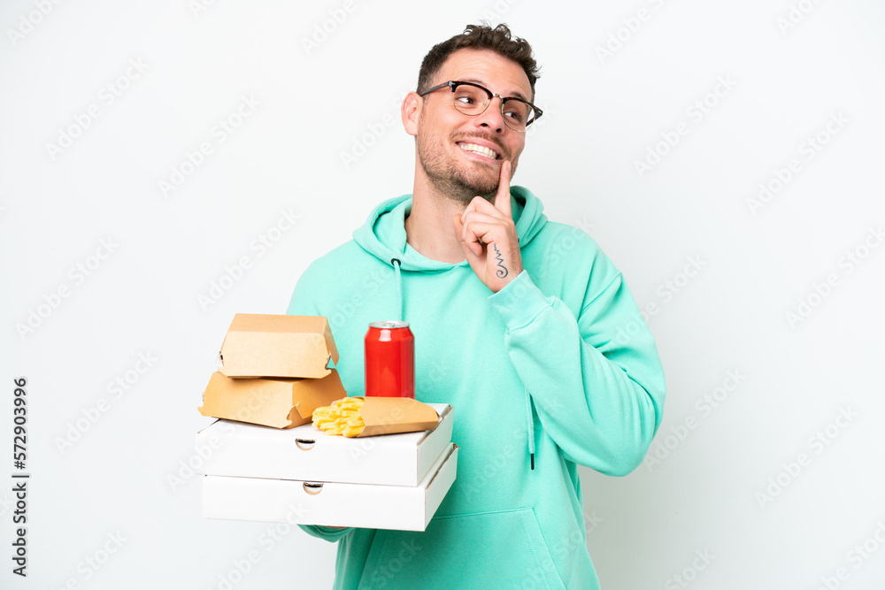 Young caucasian man holding fast food isolated on white background thinking an idea while looking up Young caucasian man holding fast food isolated on white background thinking an idea while looking up