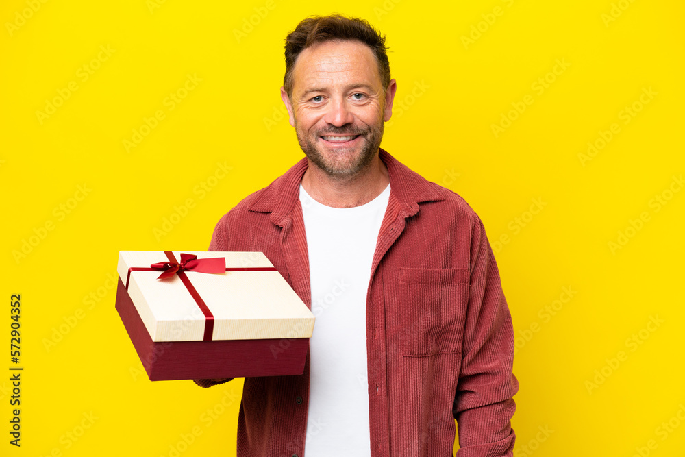 Middle age caucasian man holding a gift isolated on yellow background smiling a lot Middle age caucasian man holding a gift isolated on yellow background smiling a lot