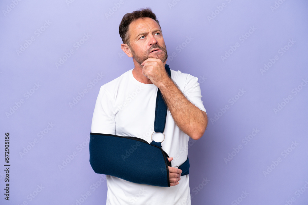 Middle age caucasian man with broken arm and wearing a sling isolated on purple background having doubts Middle age caucasian man with broken arm and wearing a sling isolated on purple background having doubts