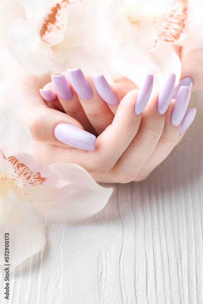 Naklejka premium Girl's hands with delicate purple manicure and orchid flowers