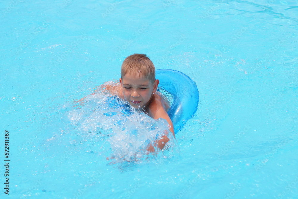 Funny little boy swims in a pool in an blue life preserver