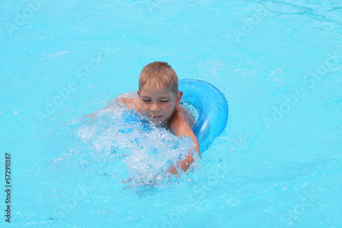 Funny little boy swims in a pool in an blue life preserver