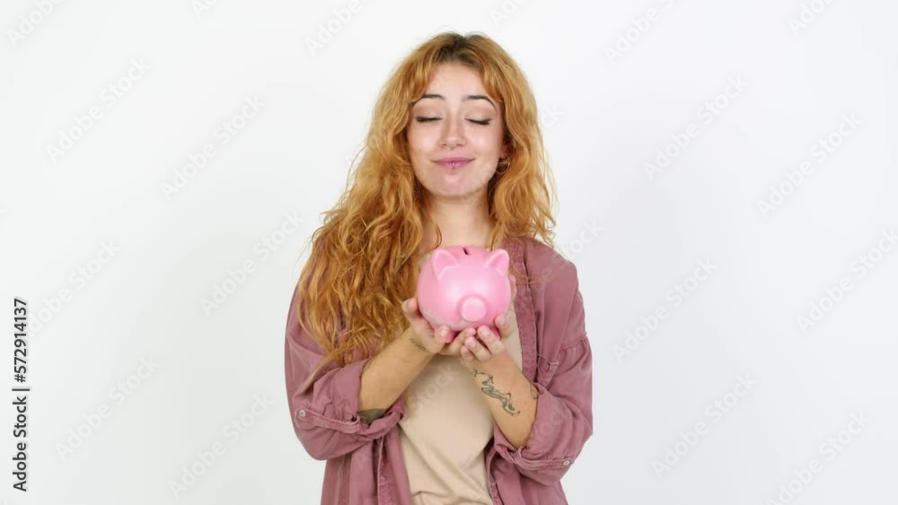 Young redhead woman unhappy and holding a piggybank over isolated background Young redhead woman unhappy and holding a piggybank over isolated background