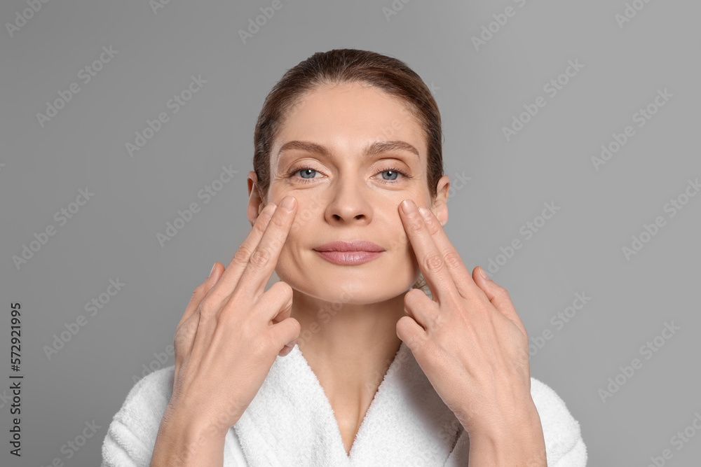 Woman massaging her face on grey background Woman massaging her face on grey background