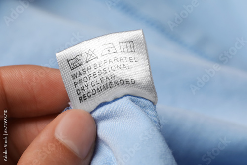 Woman holding clothing label on light blue garment, closeup