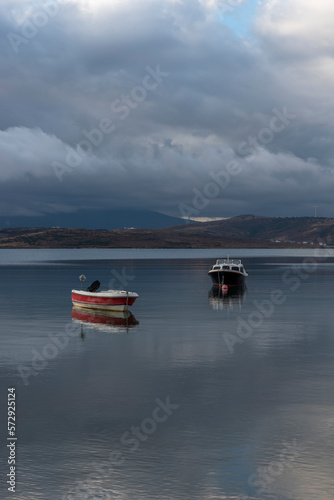 view of boat on still tranquil sea with reflection of clouds and sky on water