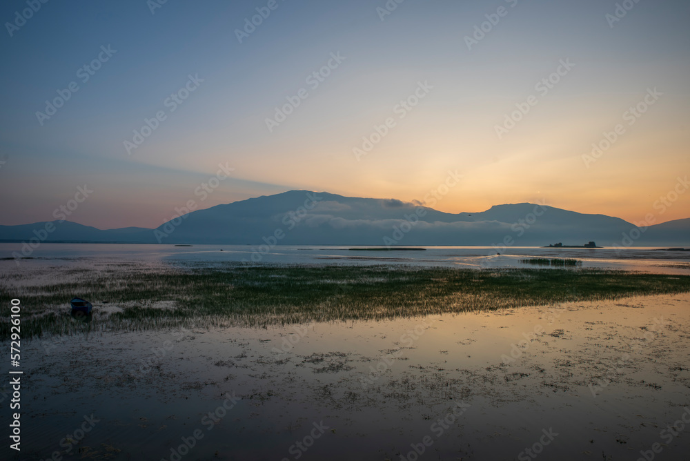View of lake isikli of denizli province at sunrise with boat on water and sun at background top of mountains