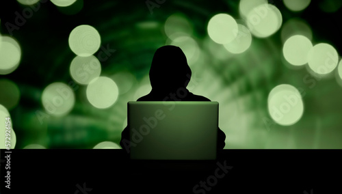 Dunkle Person mit Kapuze als Silhouette vor einem geöffneten Laptop und digit...