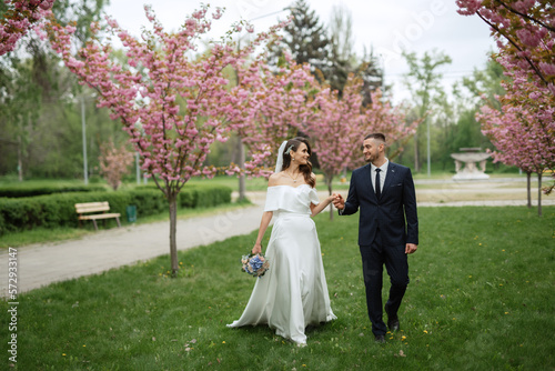 newlyweds walk in the park among cherry blossoms © omelnickiy