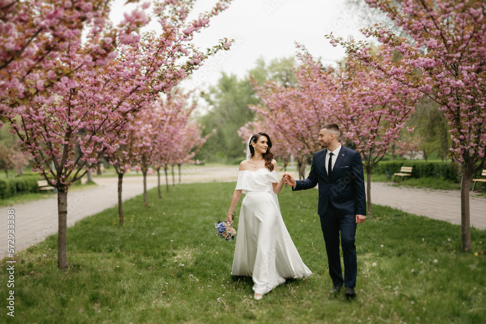 newlyweds walk in the park among cherry blossoms