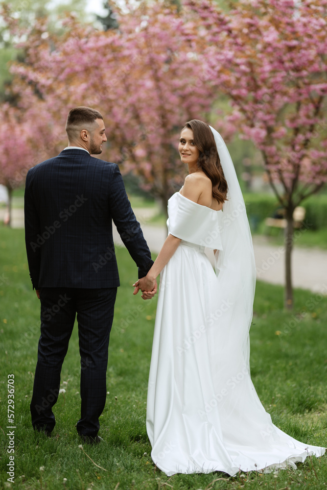newlyweds walk in the park among cherry blossoms