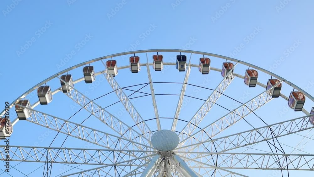 Close-up shot of colorful ferris wheel spinning on a sunny day in slow motion. 